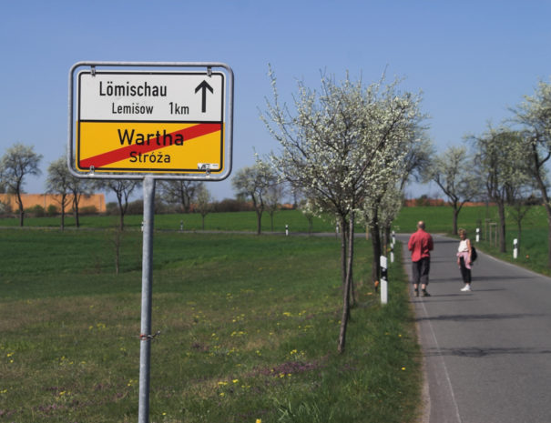 Ortsschild Wartha mit Straße und Obstbäumen daneben.